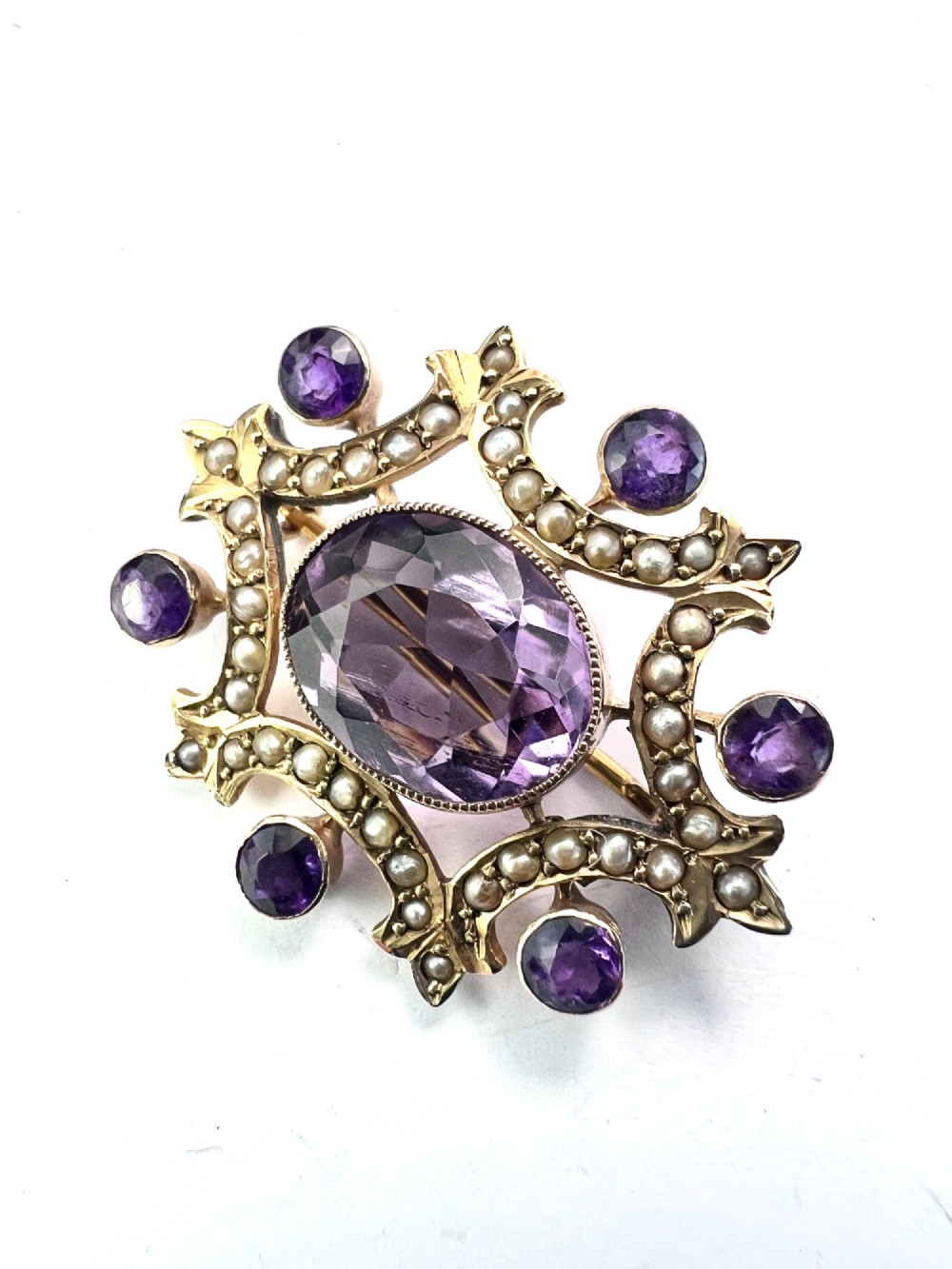 An Edwardian openwork 9ct gold brooch featuring a central oval faceted amethyst surrounded by split seed pearls and six outer round amethysts. View III