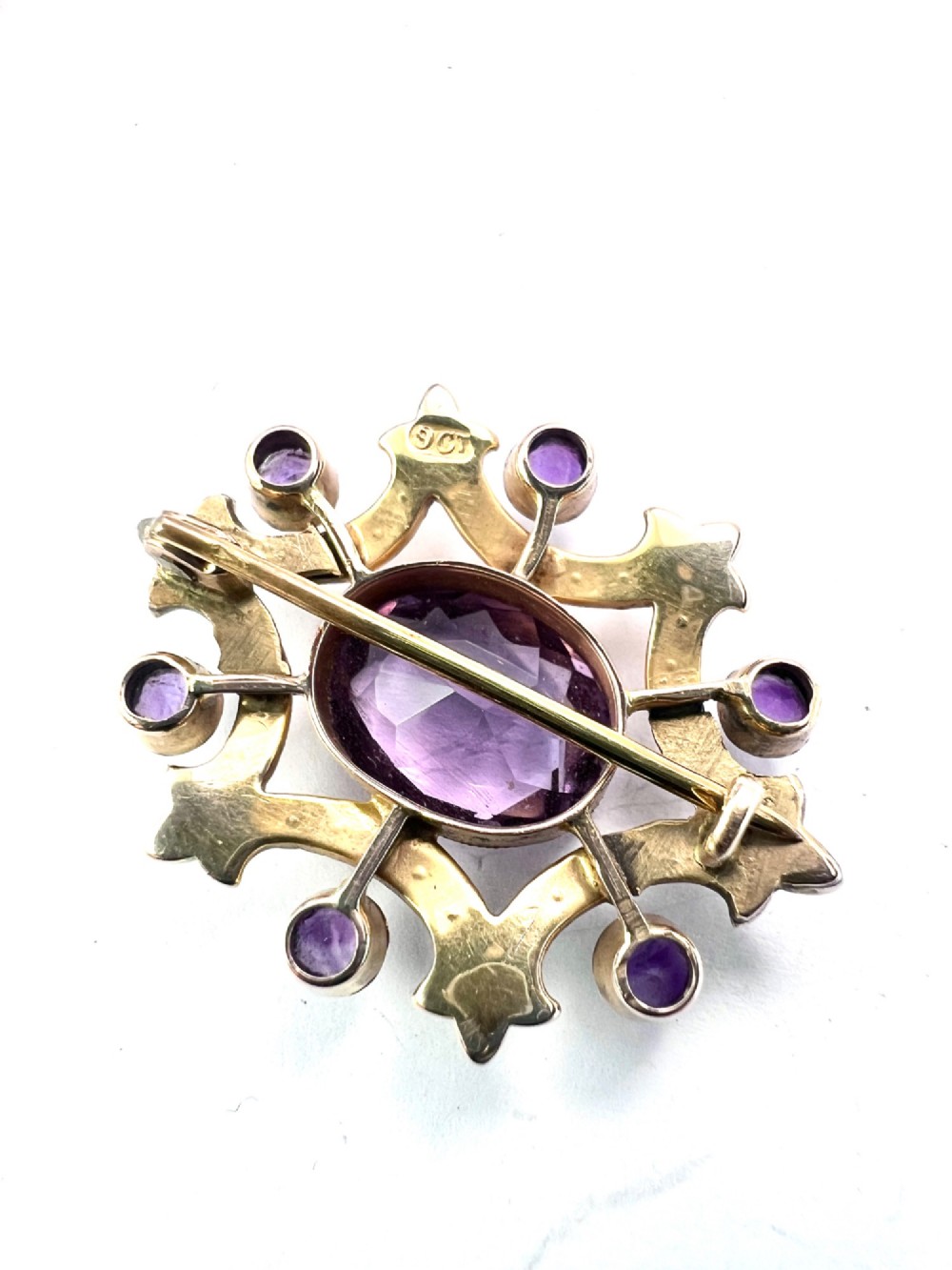 An Edwardian openwork 9ct gold brooch featuring a central oval faceted amethyst surrounded by split seed pearls and six outer round amethysts. View IV