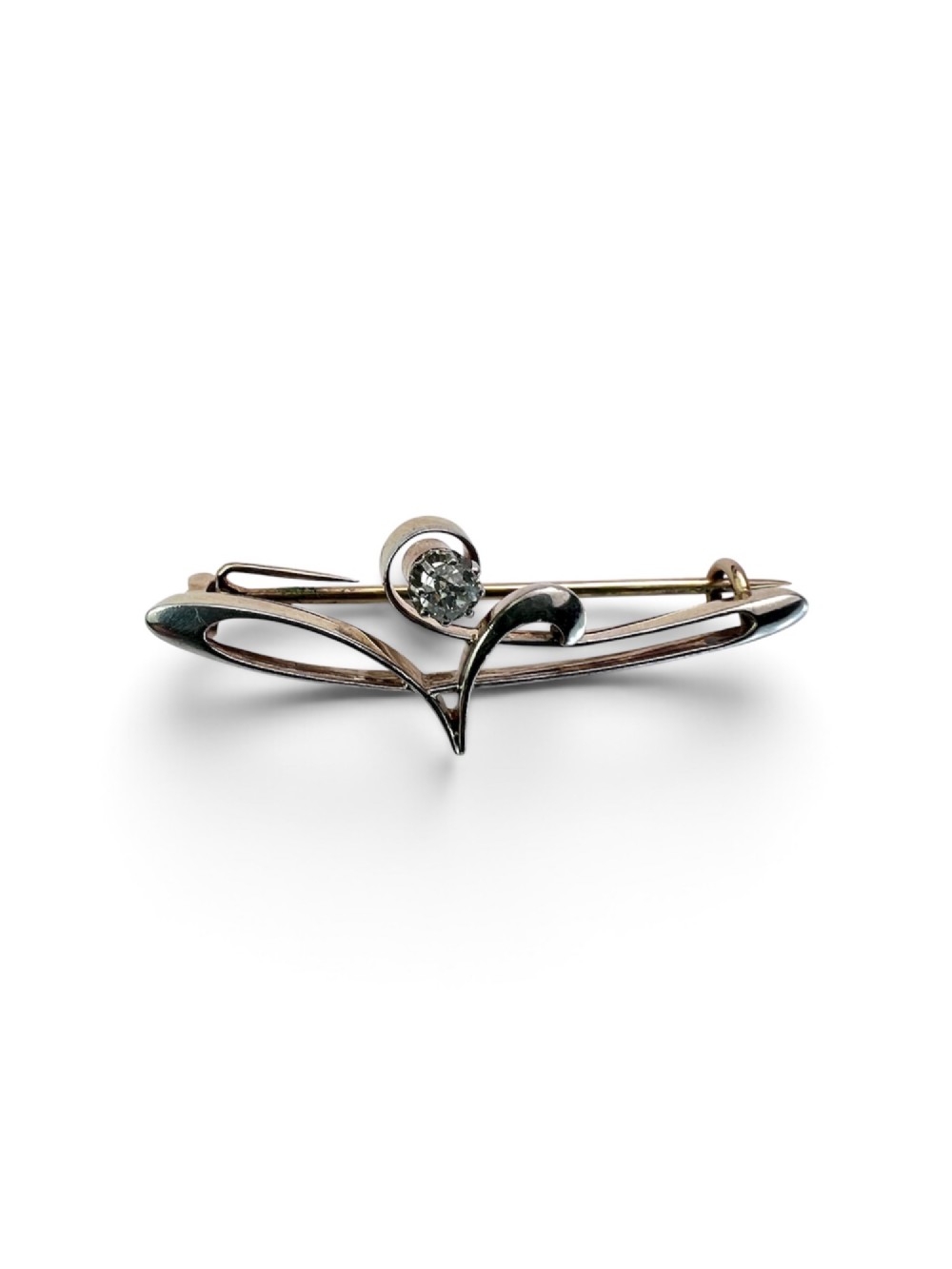 An Art Nouveau 15ct gold and platinum brooch featuring a central diamond set within fluid curvilinear metalwork, presented inside a fitted burgundy velvet box. View IV