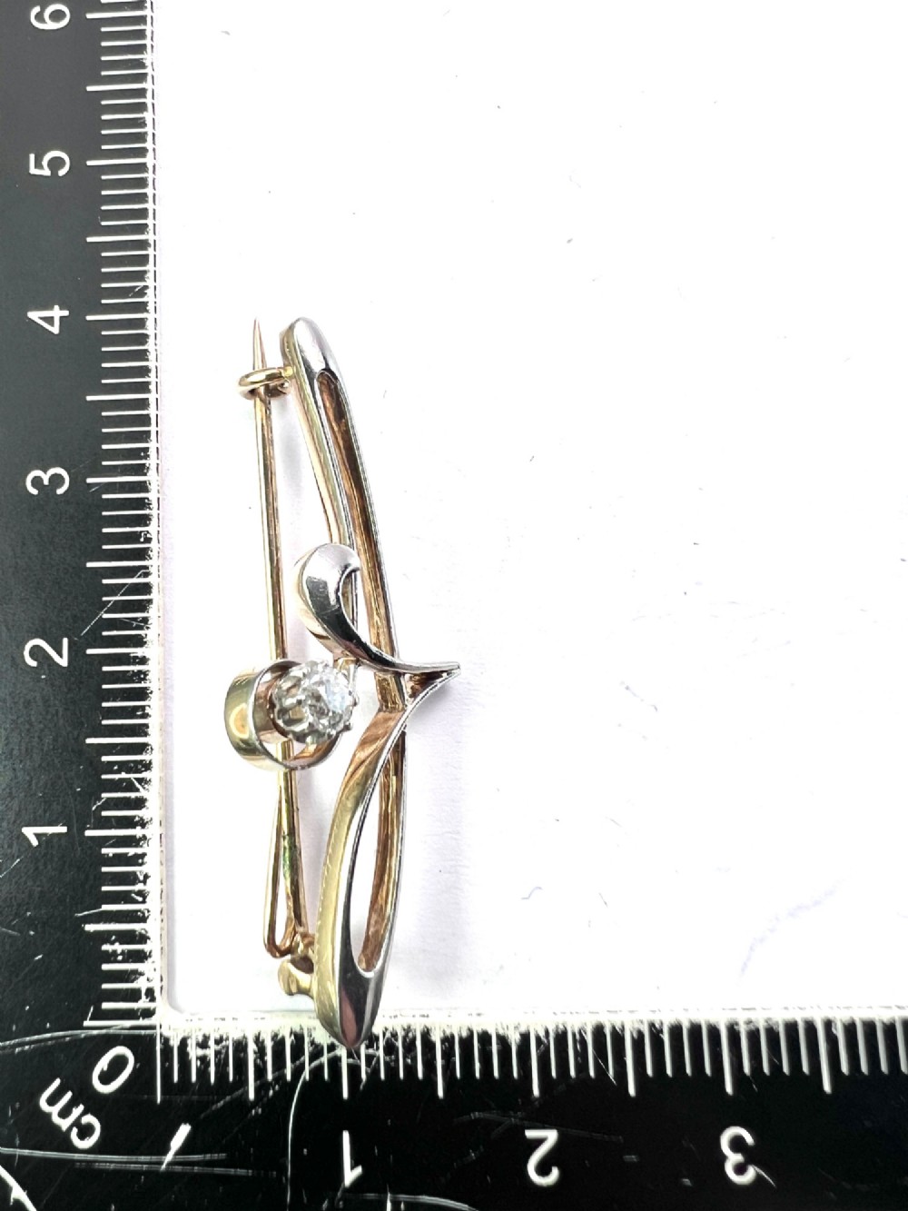 An Art Nouveau 15ct gold and platinum brooch featuring a central diamond set within fluid curvilinear metalwork, presented inside a fitted burgundy velvet box. View V