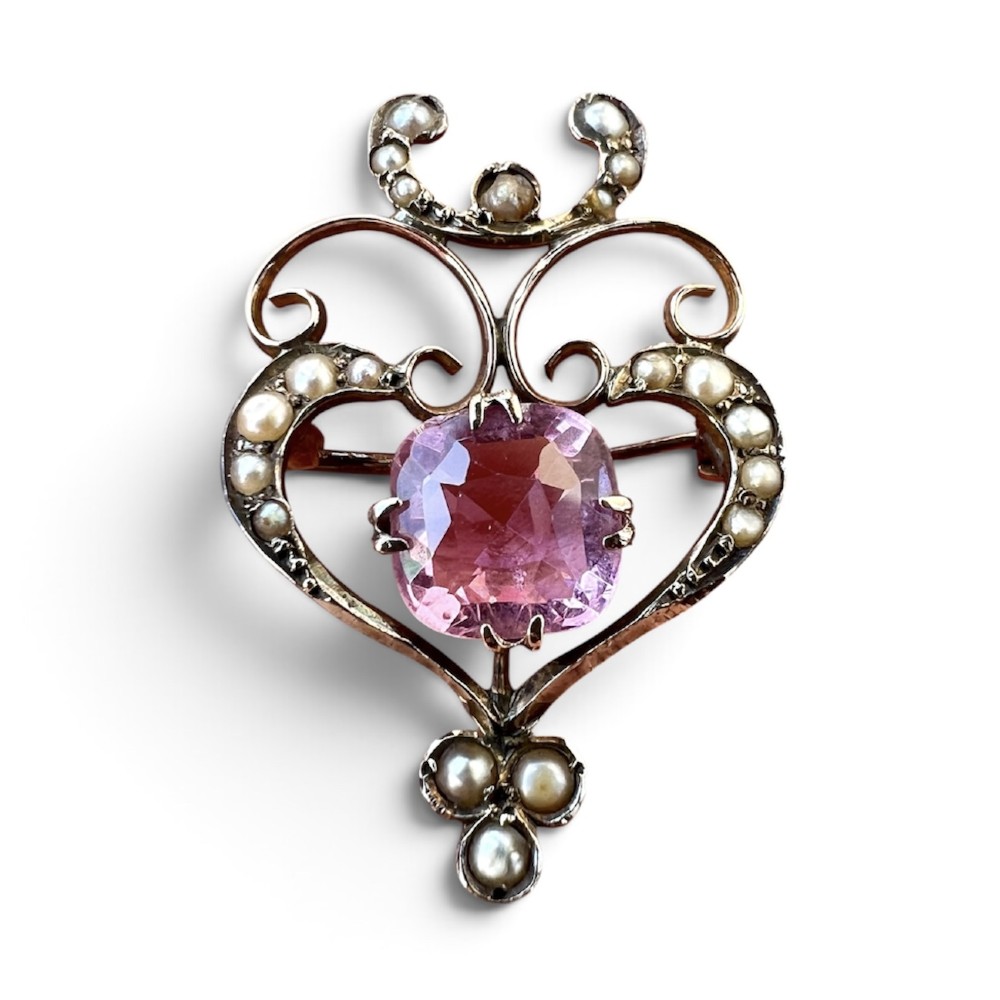 An Edwardian gold openwork scrollwork brooch featuring a central cushion-cut pink tourmaline surrounded by accent seed pearls.