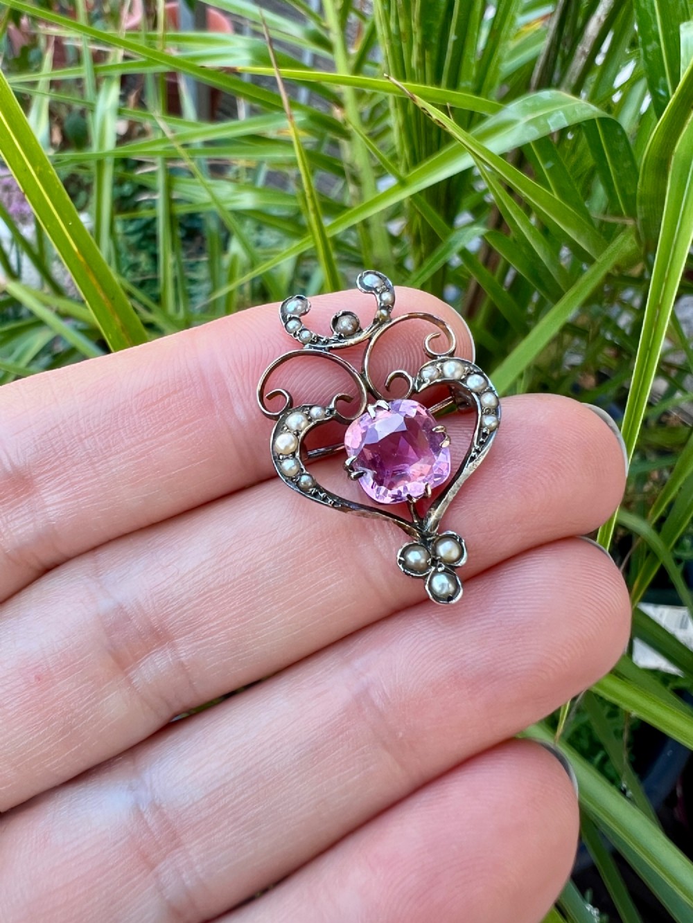 An Edwardian gold openwork scrollwork brooch featuring a central cushion-cut pink tourmaline surrounded by accent seed pearls. View V