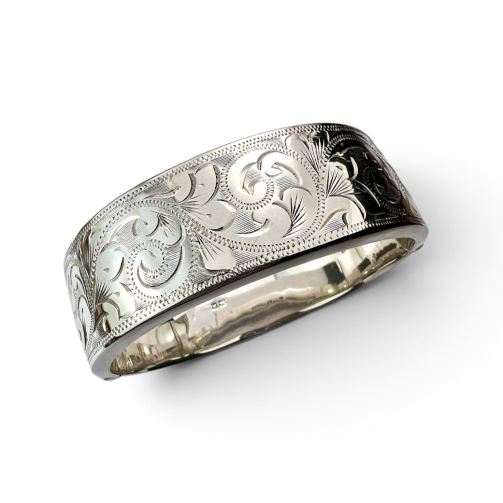 A wide sterling silver hinged bangle featuring detailed hand-engraved scrollwork and a polished inner finish.