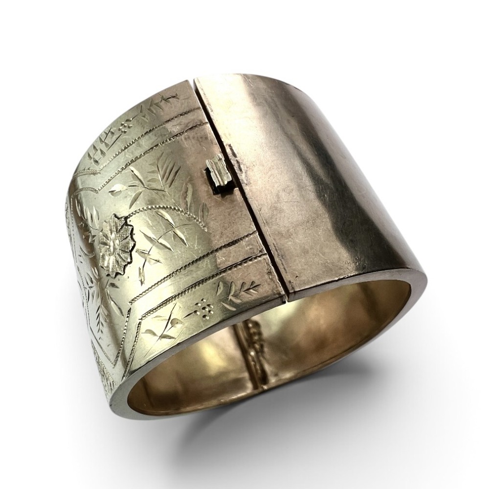 A wide Victorian sterling silver hinged cuff bangle featuring hand-engraved floral and geometric patterns across the exterior surface. View IV