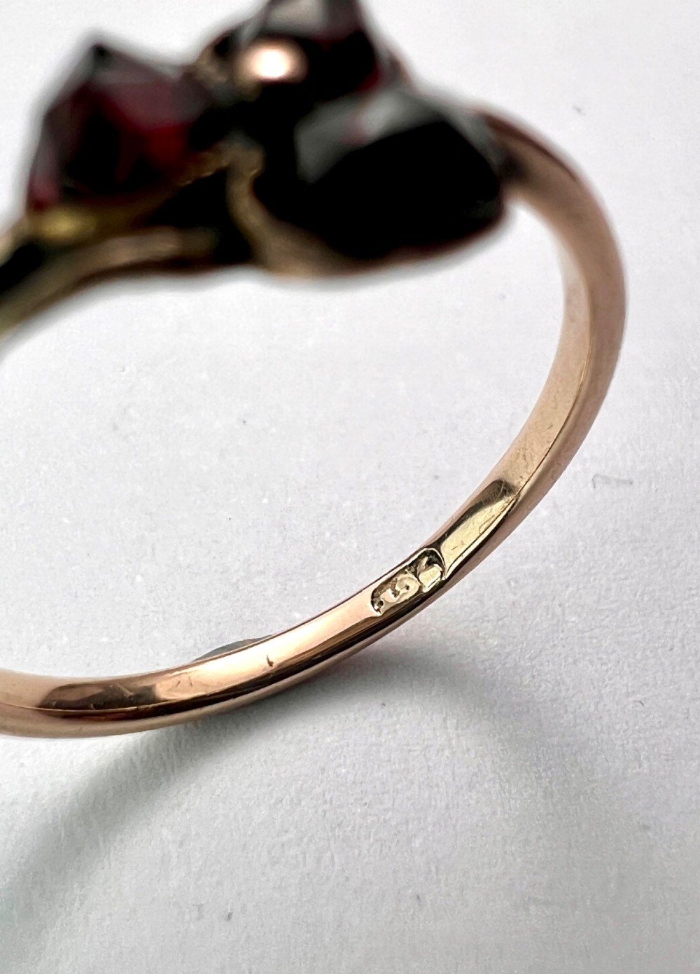 A Victorian 9ct gold ring featuring three deep red garnets arranged in a floral design set upon a slim band. View VII
