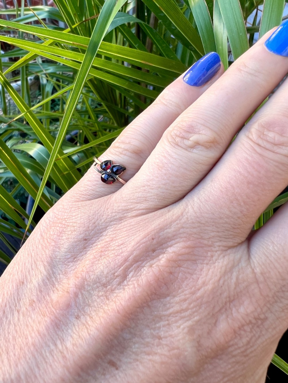 A Victorian 9ct gold ring featuring three deep red garnets arranged in a floral design set upon a slim band. View VIII