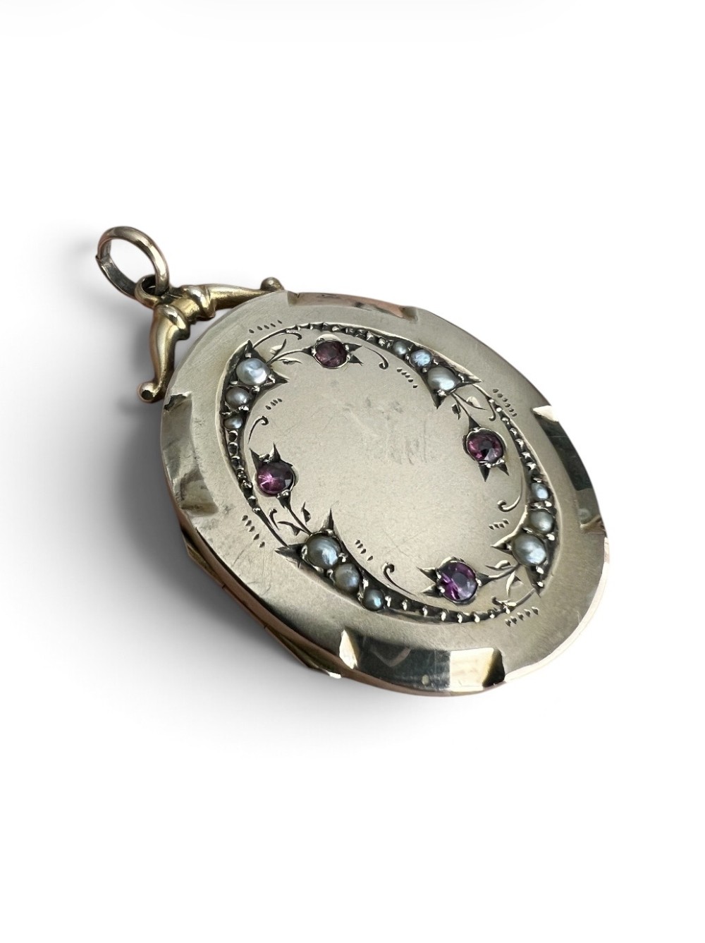 An oval 9ct yellow gold Victorian locket decorated with foliate engraving and inlaid with rubies and seed pearls. View II