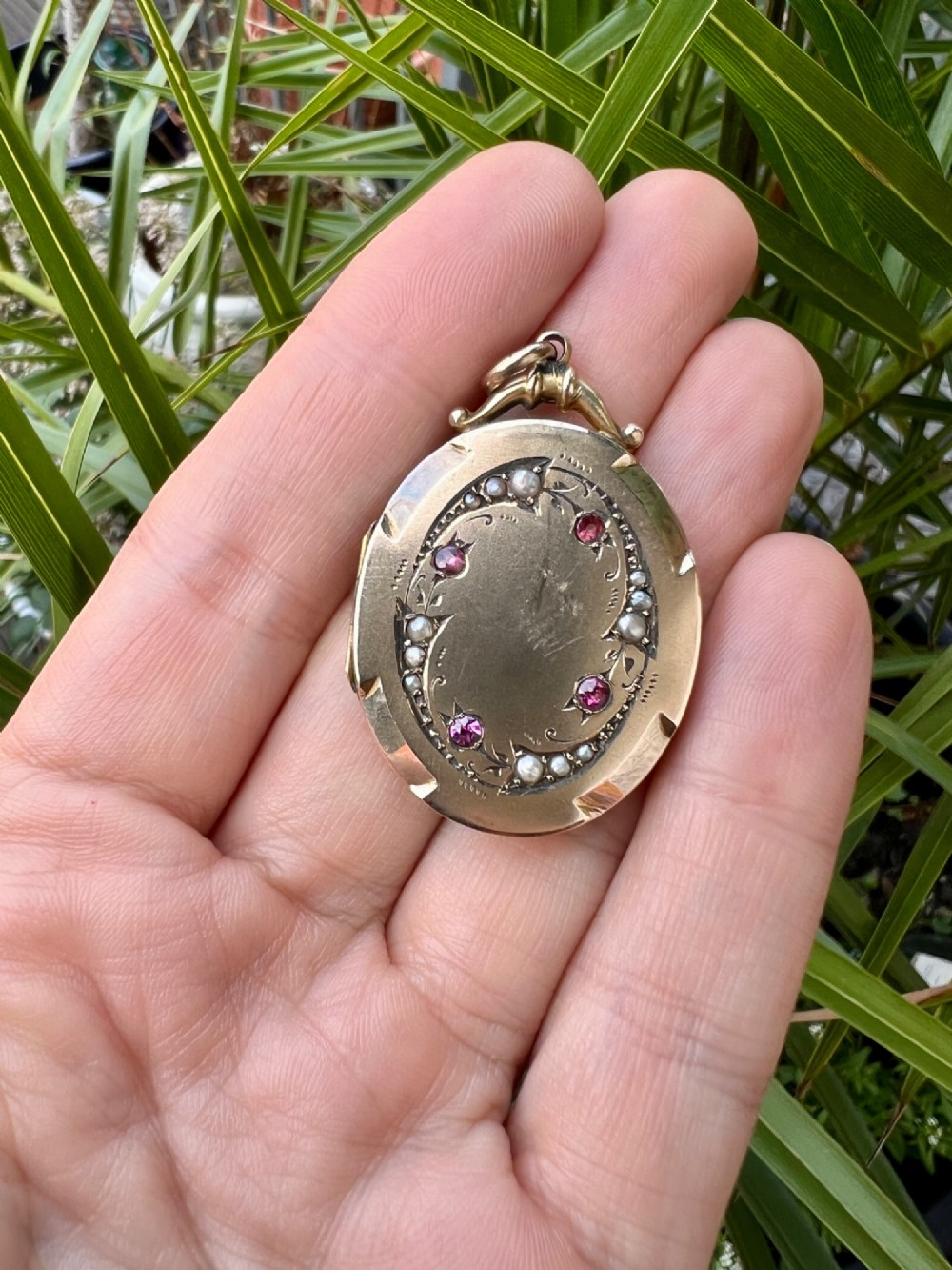 An oval 9ct yellow gold Victorian locket decorated with foliate engraving and inlaid with rubies and seed pearls. View VII