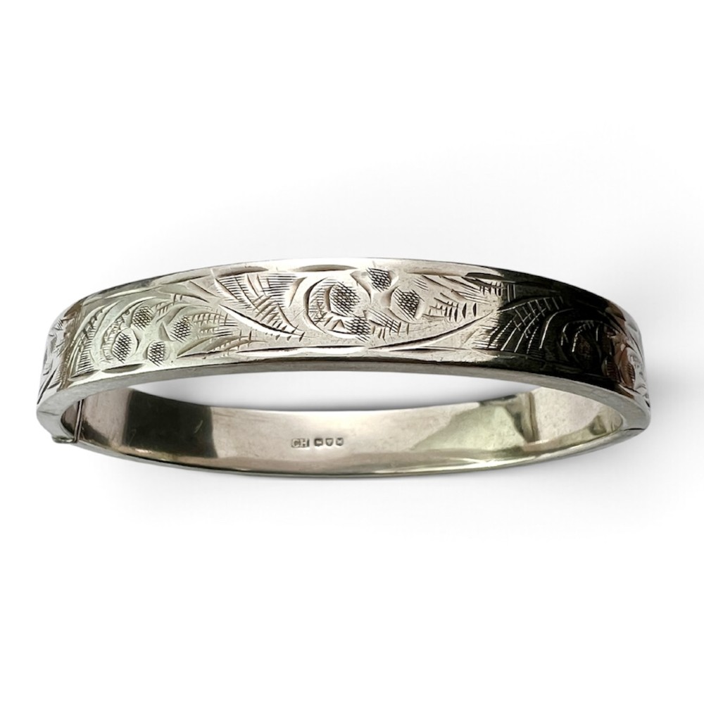 A sterling silver hinged bangle decorated with engraved foliate motifs and visible internal makers hallmarks.