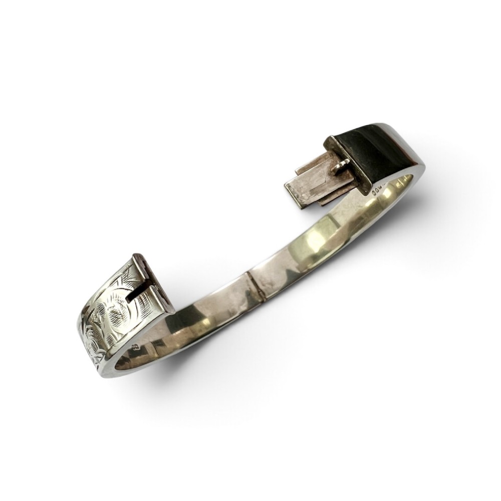 A sterling silver hinged bangle decorated with engraved foliate motifs and visible internal makers hallmarks. View V