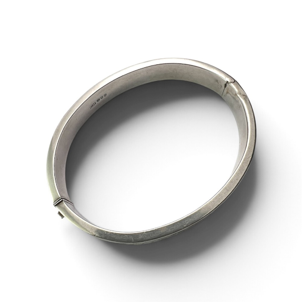A sterling silver hinged bangle decorated with engraved foliate motifs and visible internal makers hallmarks. View VI