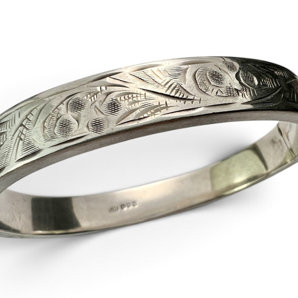 A sterling silver hinged bangle decorated with engraved foliate motifs and visible internal makers hallmarks. View VII
