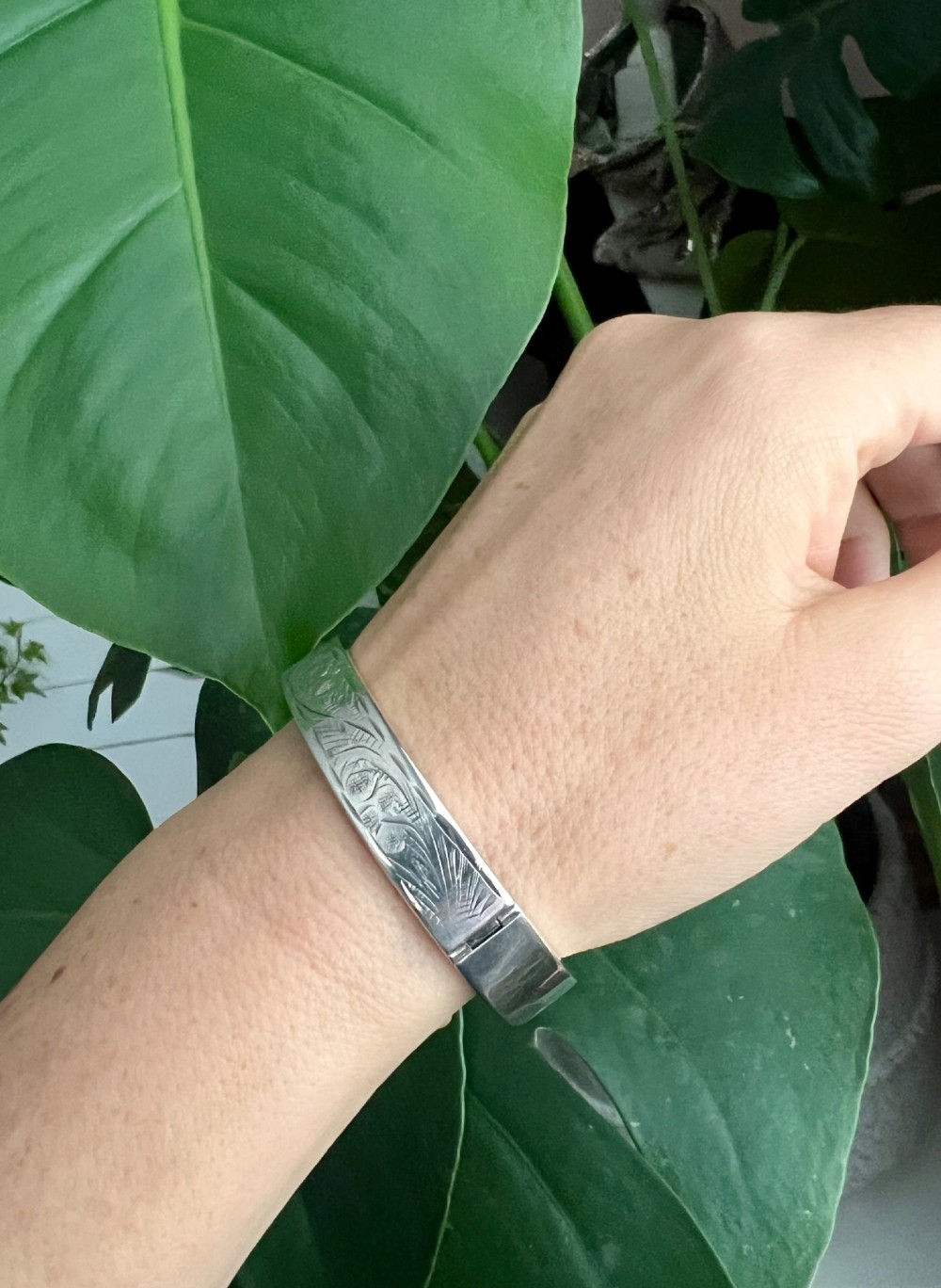 A sterling silver hinged bangle decorated with engraved foliate motifs and visible internal makers hallmarks. View X