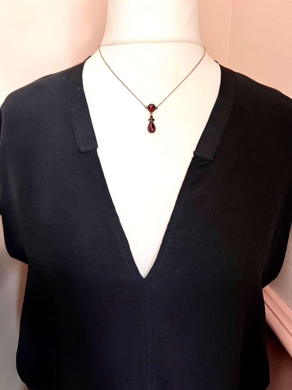 An antique Victorian necklace featuring a fine metal chain holding a drop pendant set with multiple faceted deep red garnets. View VI