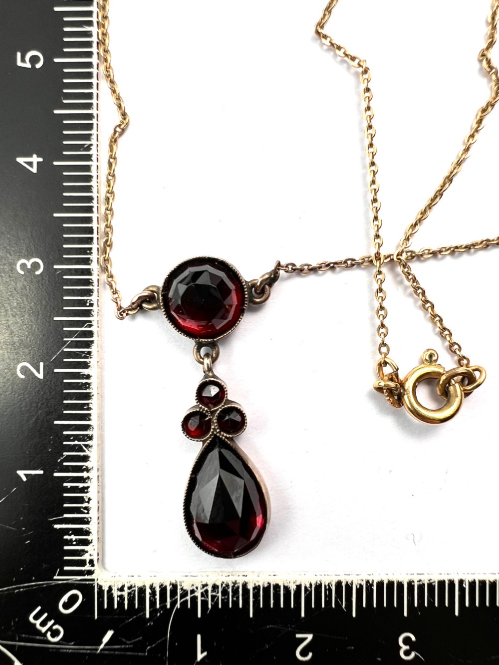 An antique Victorian necklace featuring a fine metal chain holding a drop pendant set with multiple faceted deep red garnets. View VII