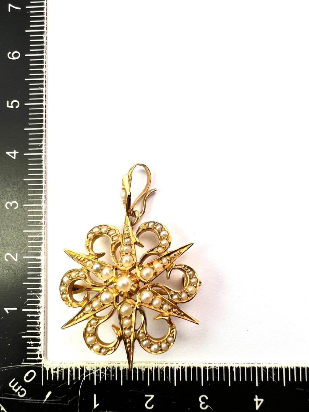 An antique 15ct yellow gold sunburst pendant brooch set with seed pearls arranged in a celestial starburst and scroll motif. View VII