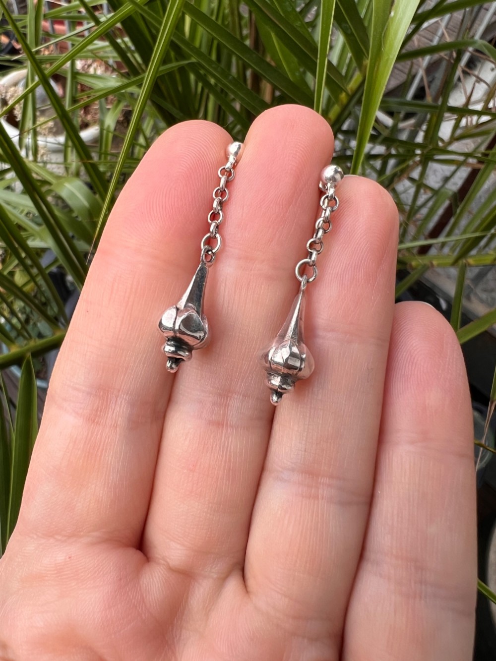 A pair of sterling silver drop earrings featuring screw-back fastenings, chain links, and ribbed lotus bud pendants. View V