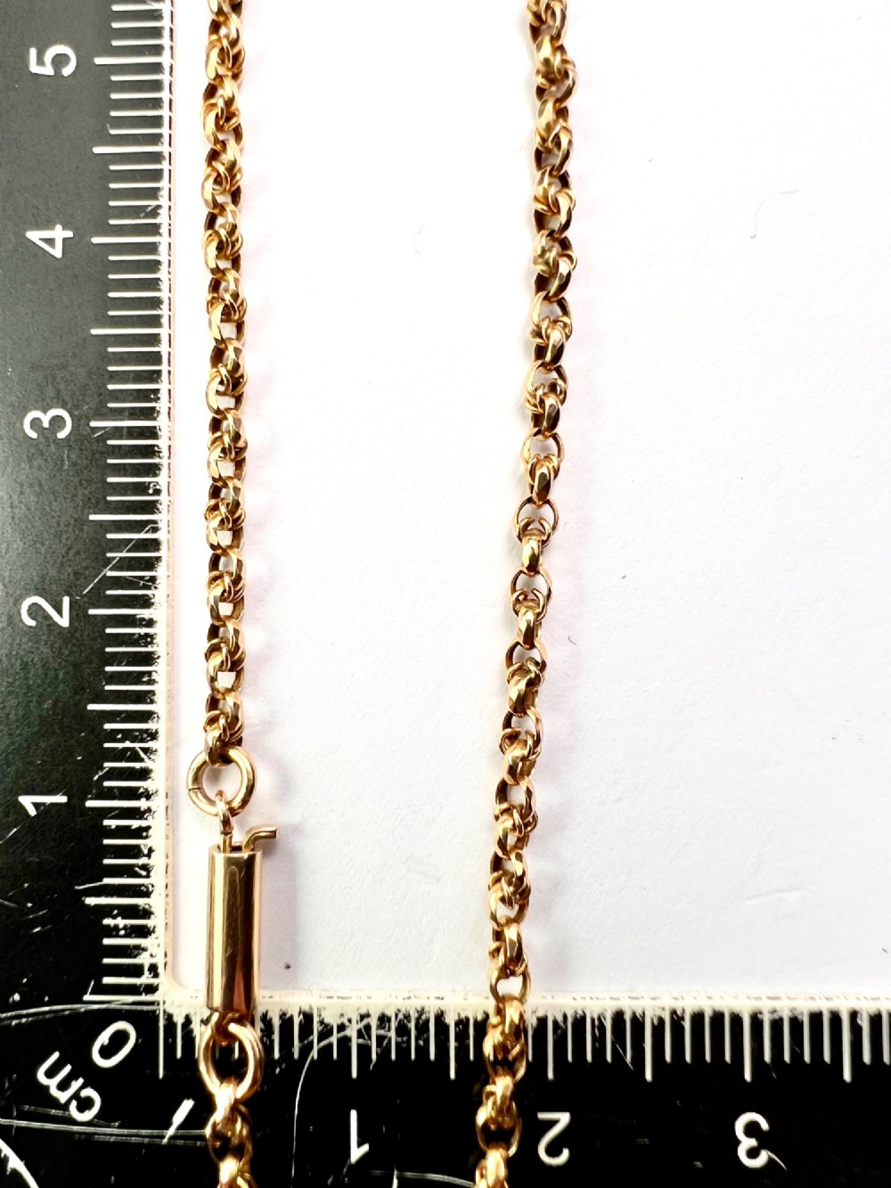 An Edwardian 9ct gold chain necklace coiled flat against a neutral white background displaying rope links and a cylindrical clasp. View VII