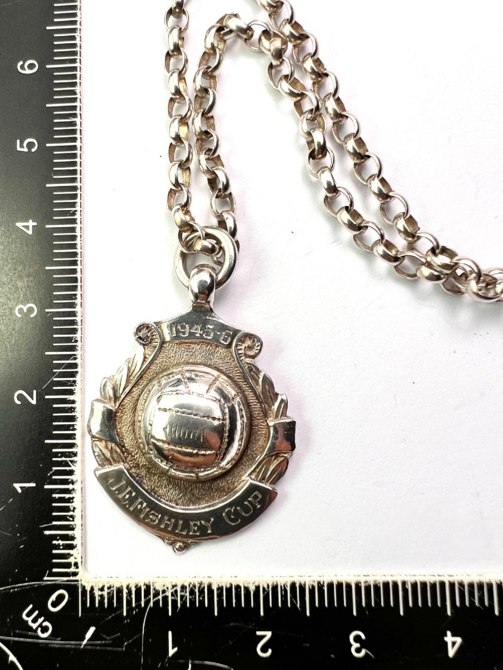 A sterling silver chain necklace featuring a shield-shaped football medal pendant engraved with 1945-6 and JR Fishley Cup. View II