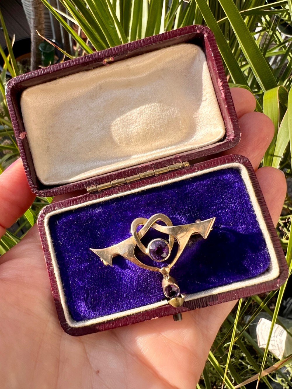 An Art Nouveau 9ct gold brooch featuring a heart-shaped whiplash frame set with a round purple amethyst and a suspended amethyst drop, displayed inside a fitted velvet case. View VII