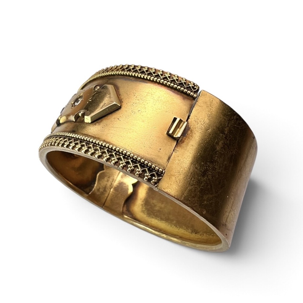A wide Victorian Etruscan Revival gold hinged bangle decorated with intricate beadwork borders and star-set gemstones across a central band. View II