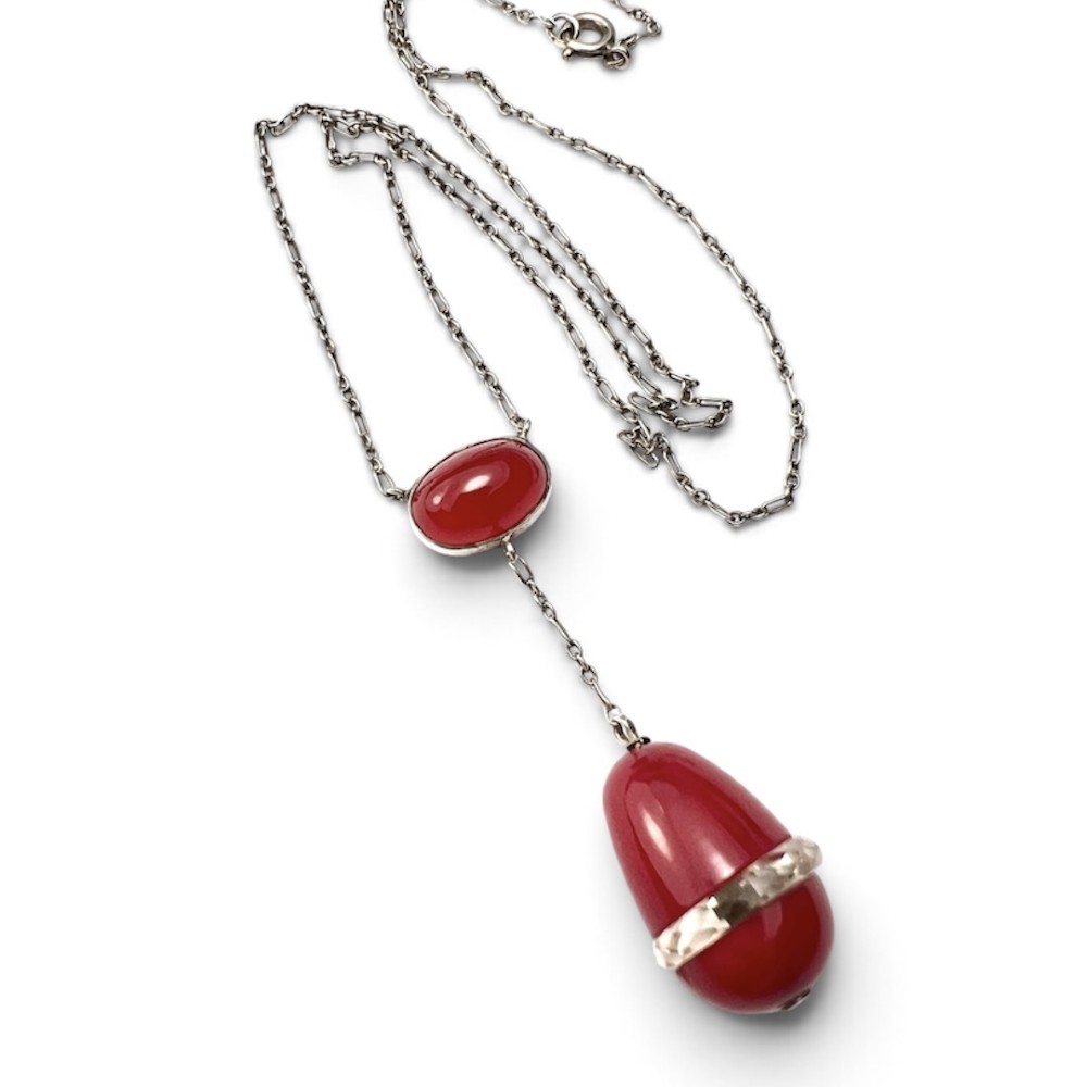 An Edwardian silver lavalier necklace featuring an oval red stone cabochon and an egg-shaped red pendant bound by a silver band.