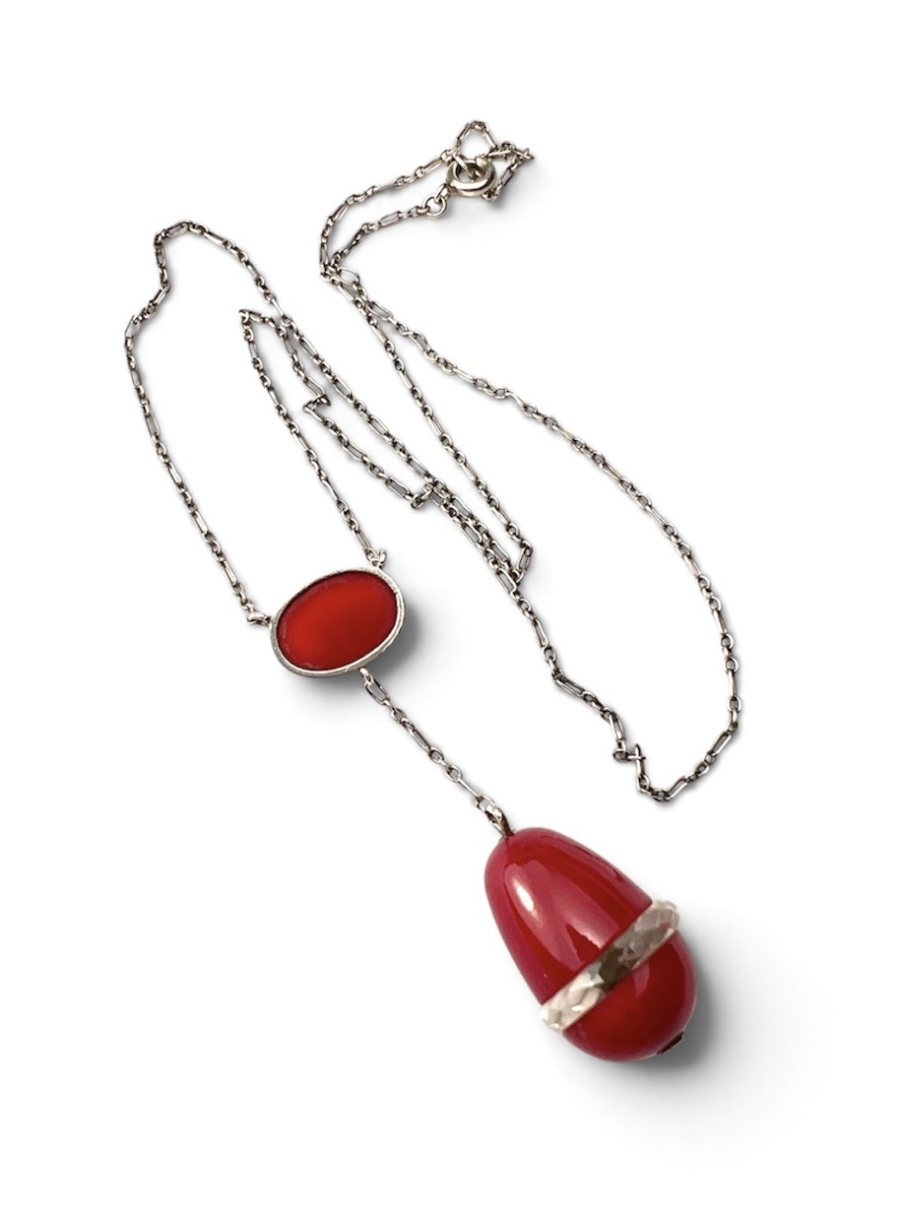 An Edwardian silver lavalier necklace featuring an oval red stone cabochon and an egg-shaped red pendant bound by a silver band. View V