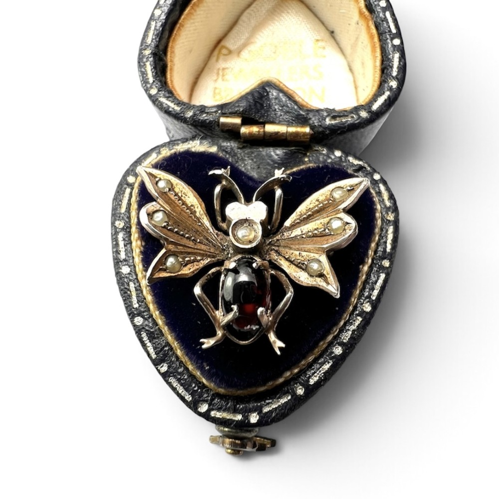 A Victorian silver gilt brooch shaped like an insect, featuring a cabochon red garnet body and wings accented with small seed pearls. View II