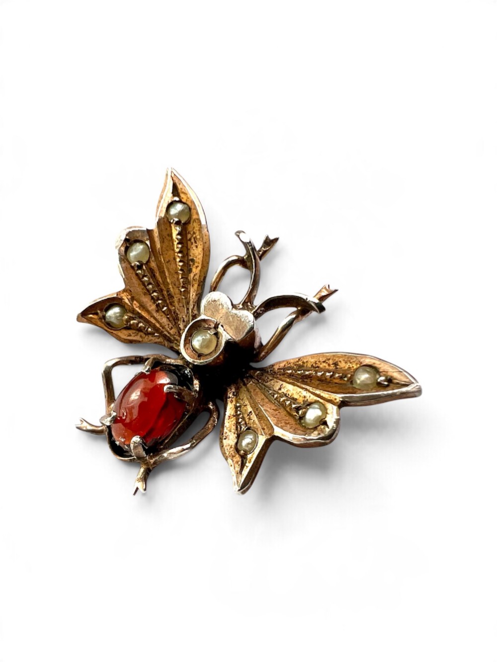 A Victorian silver gilt brooch shaped like an insect, featuring a cabochon red garnet body and wings accented with small seed pearls. View V