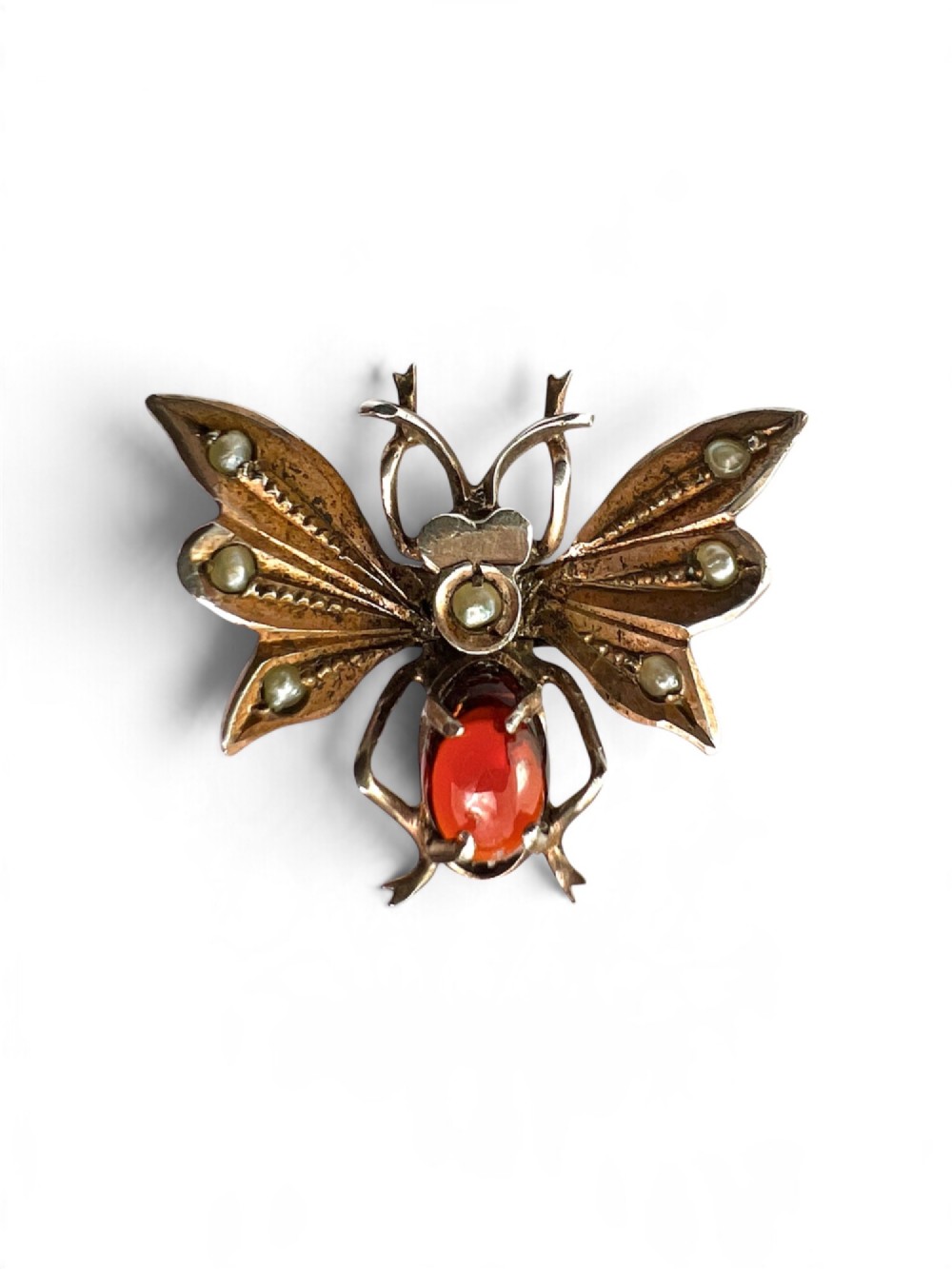 A Victorian silver gilt brooch shaped like an insect, featuring a cabochon red garnet body and wings accented with small seed pearls. View VI