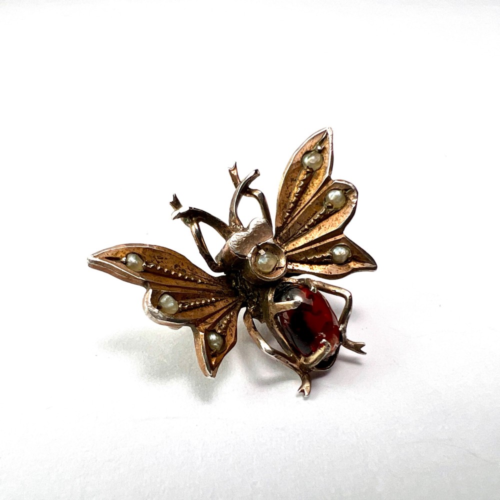 A Victorian silver gilt brooch shaped like an insect, featuring a cabochon red garnet body and wings accented with small seed pearls. View VII