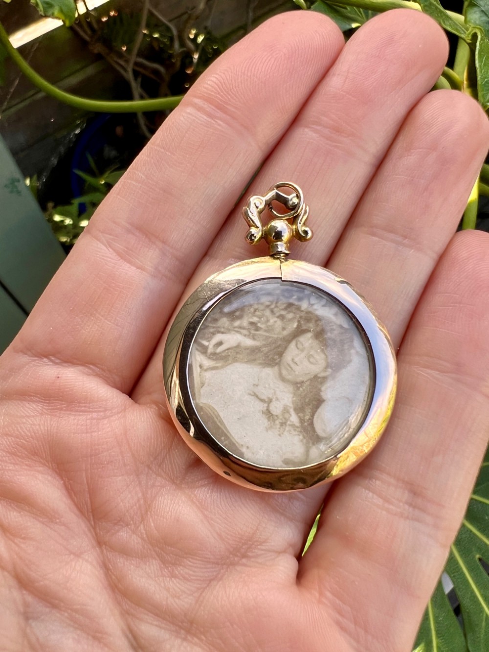 A circular Edwardian 9ct gold screw-top photo locket with an ornate scroll bail housing a sepia portrait photograph behind glass. View V