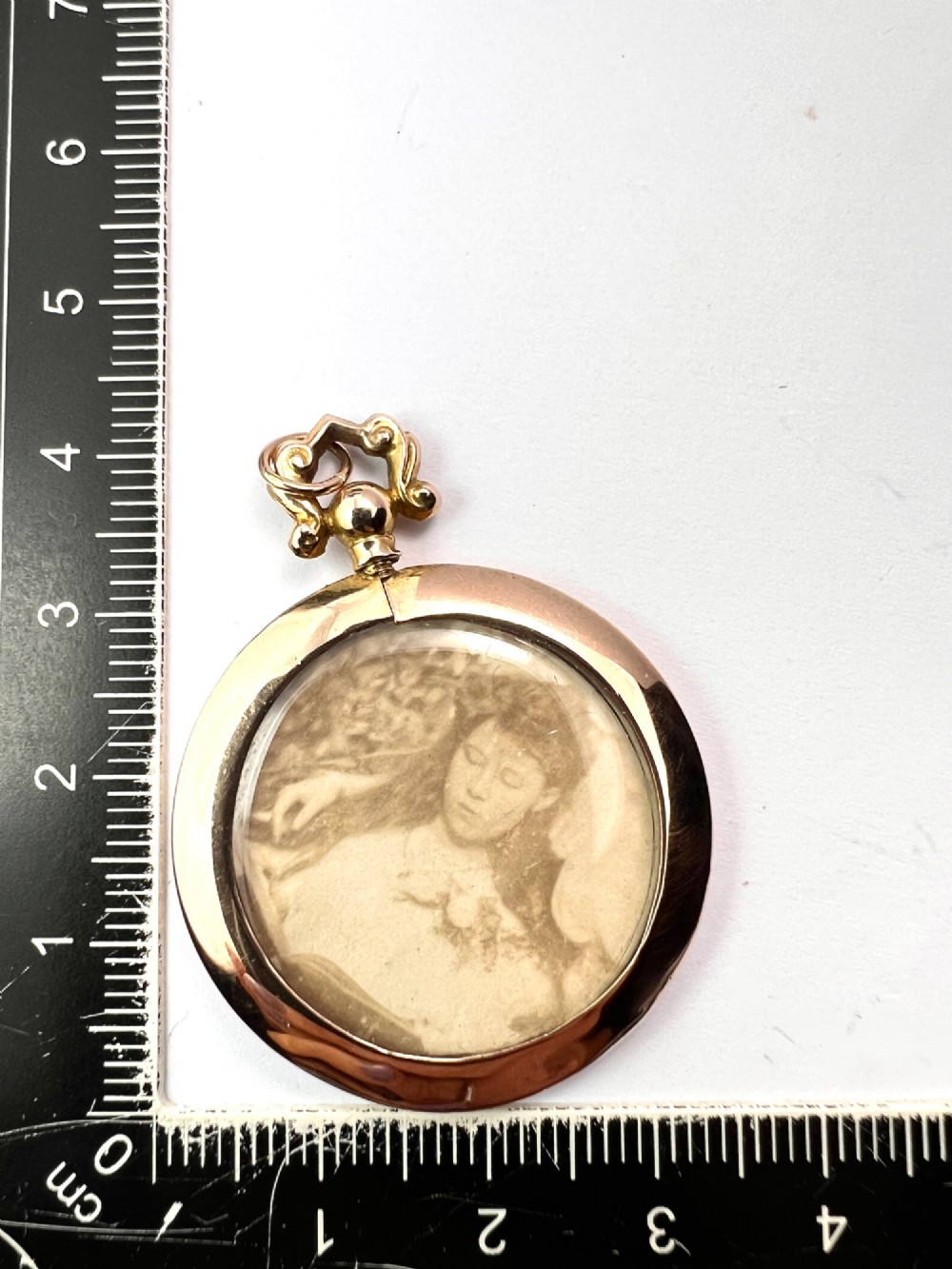 A circular Edwardian 9ct gold screw-top photo locket with an ornate scroll bail housing a sepia portrait photograph behind glass. View VI