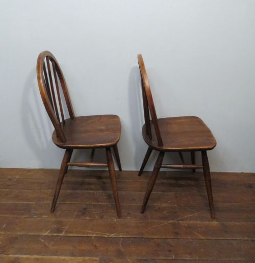 fig 1. A pair of warm brown wooden dining chairs featuring hoop-shaped spindle backs, contoured elm seats, and splayed legs.