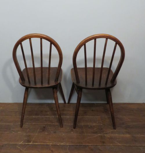 fig 2. A pair of warm brown wooden dining chairs featuring hoop-shaped spindle backs, contoured elm seats, and splayed legs.
