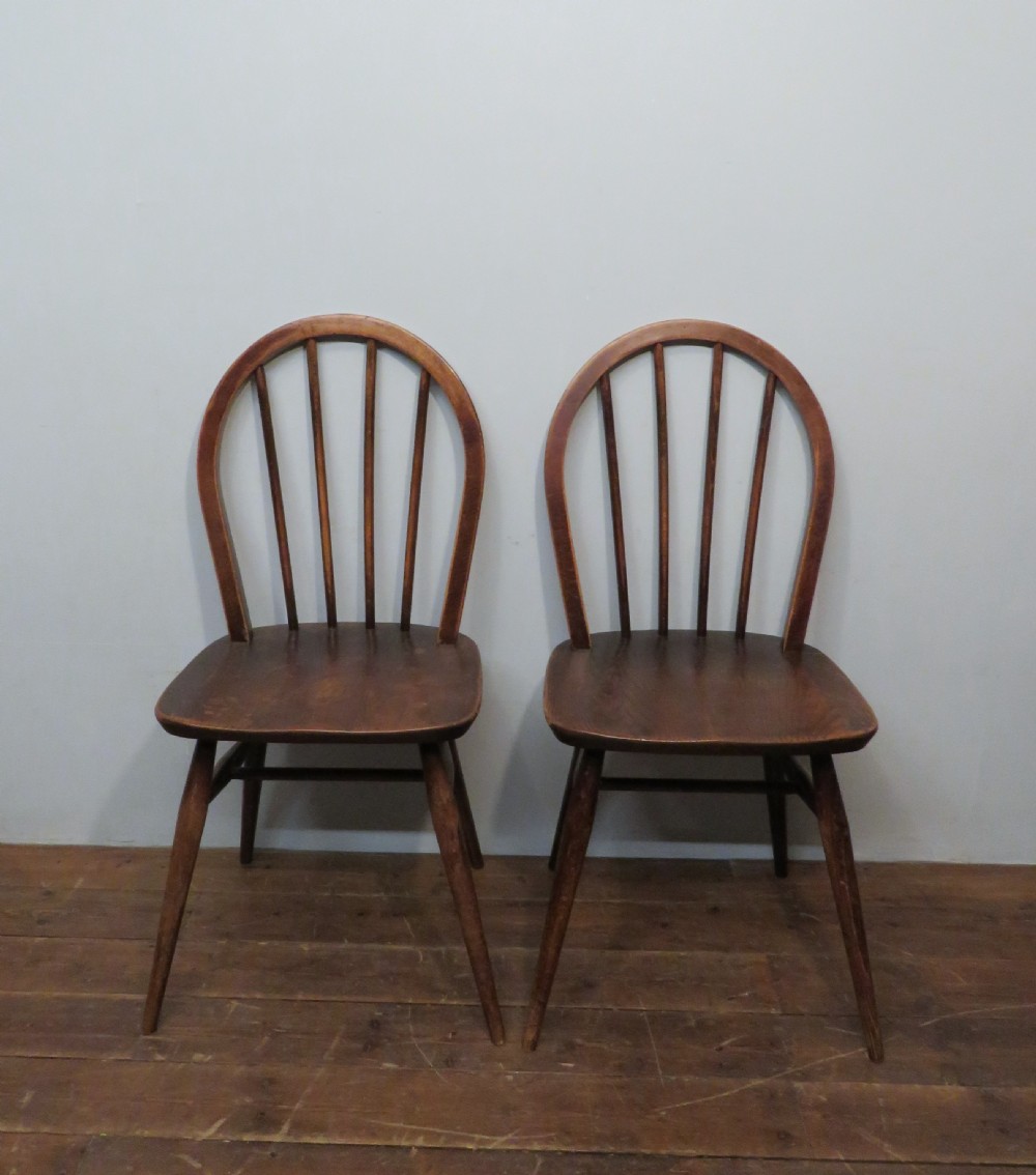 A pair of warm brown wooden dining chairs featuring hoop-shaped spindle backs, contoured elm seats, and splayed legs.
