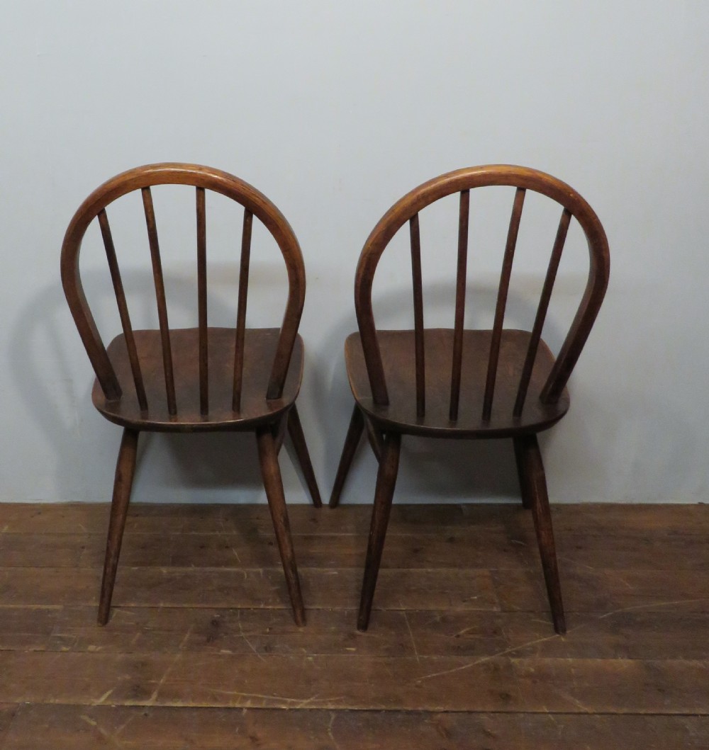 A pair of warm brown wooden dining chairs featuring hoop-shaped spindle backs, contoured elm seats, and splayed legs. View III
