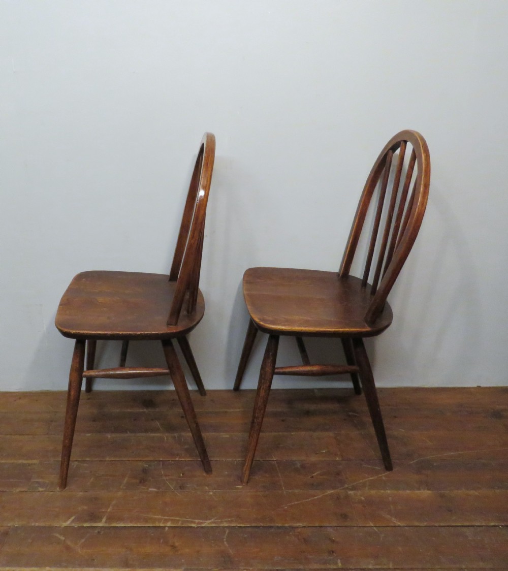 A pair of warm brown wooden dining chairs featuring hoop-shaped spindle backs, contoured elm seats, and splayed legs. View IV