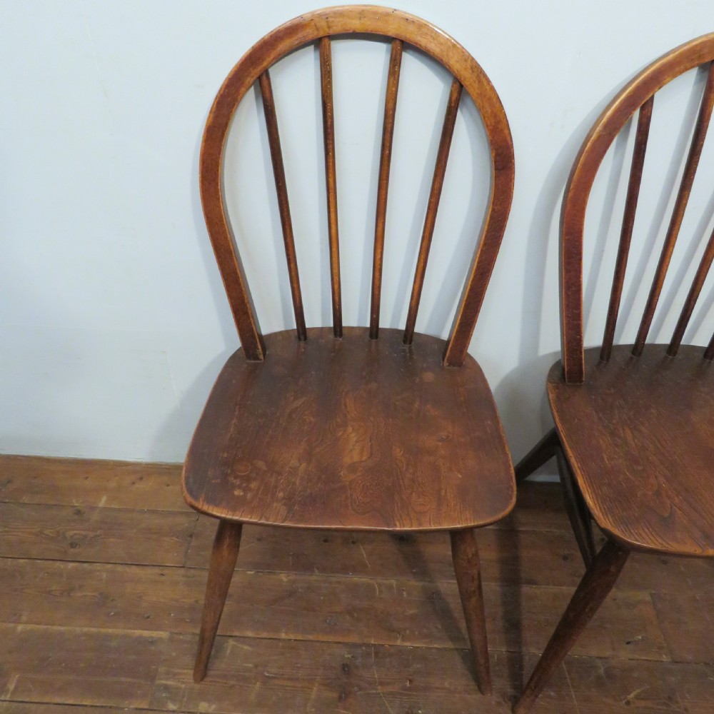 A pair of warm brown wooden dining chairs featuring hoop-shaped spindle backs, contoured elm seats, and splayed legs. View V