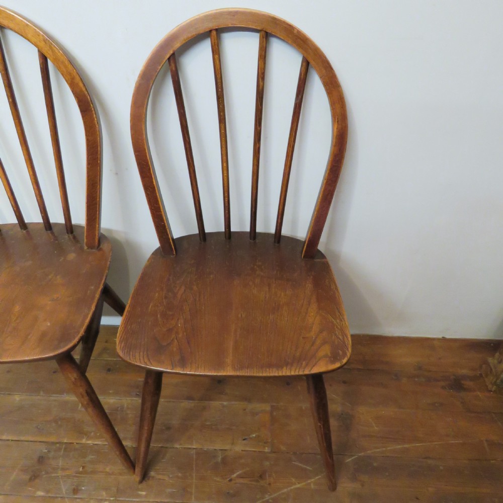 A pair of warm brown wooden dining chairs featuring hoop-shaped spindle backs, contoured elm seats, and splayed legs. View VI
