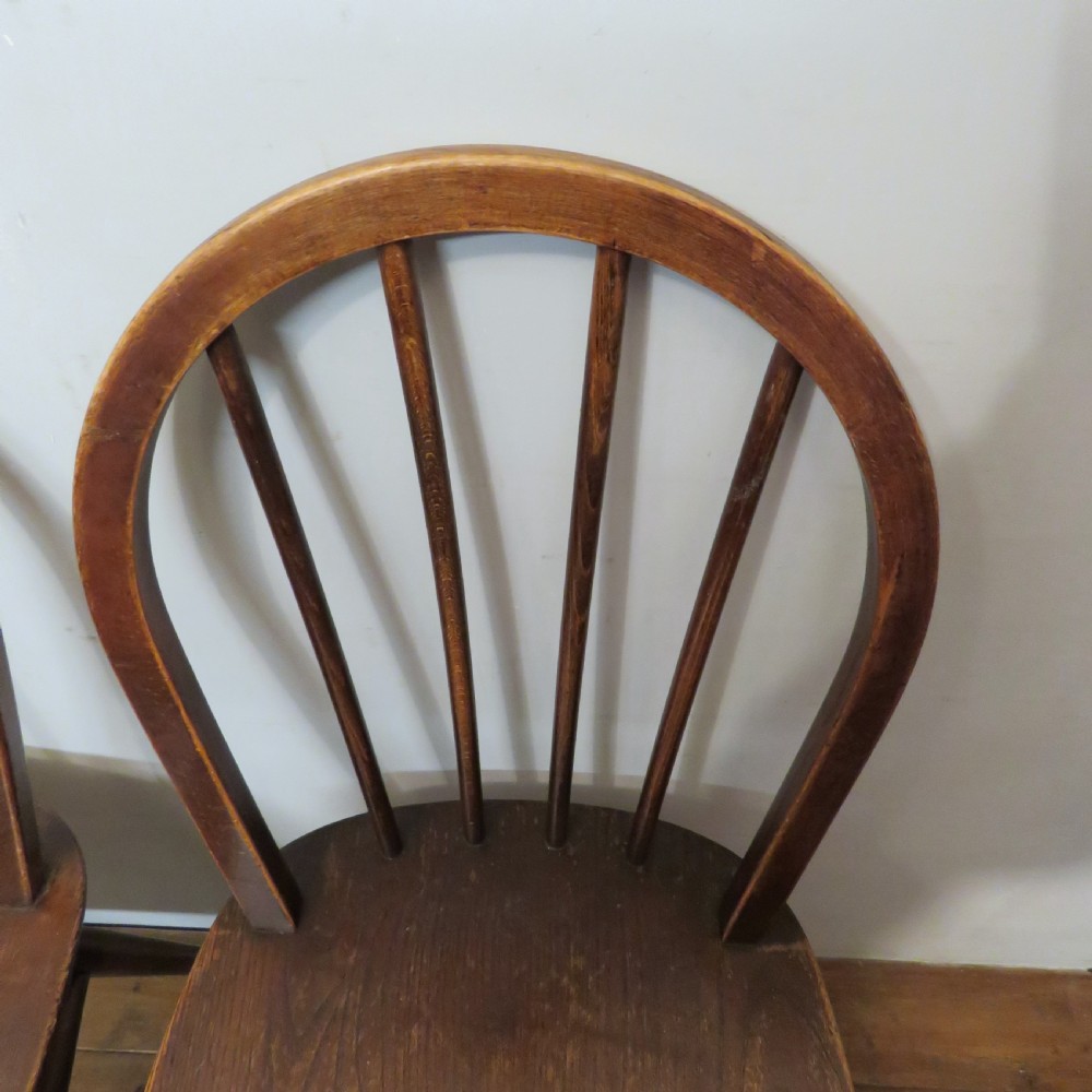 A pair of warm brown wooden dining chairs featuring hoop-shaped spindle backs, contoured elm seats, and splayed legs. View VII