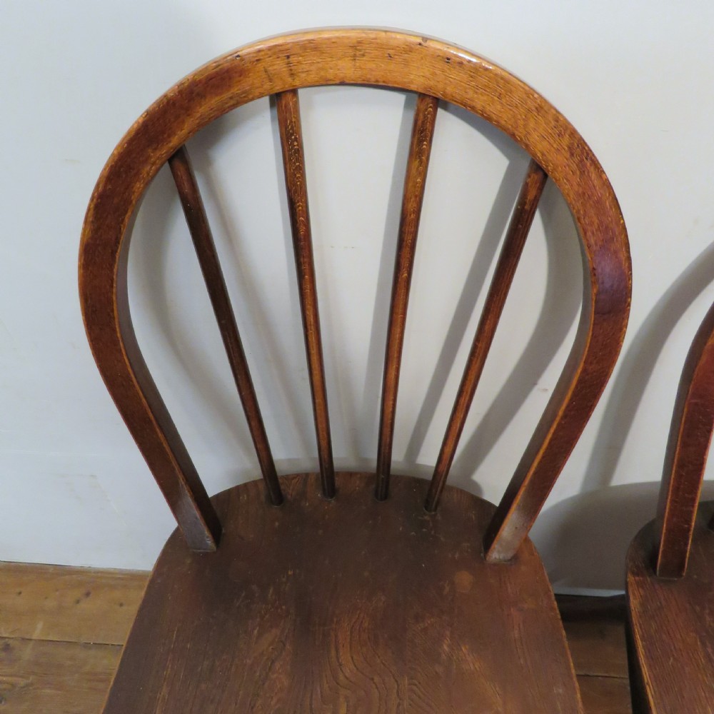 A pair of warm brown wooden dining chairs featuring hoop-shaped spindle backs, contoured elm seats, and splayed legs. View VIII