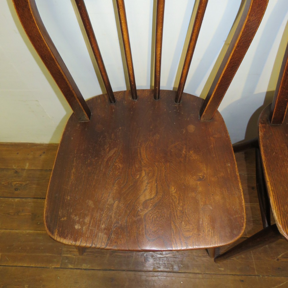 A pair of warm brown wooden dining chairs featuring hoop-shaped spindle backs, contoured elm seats, and splayed legs. View X