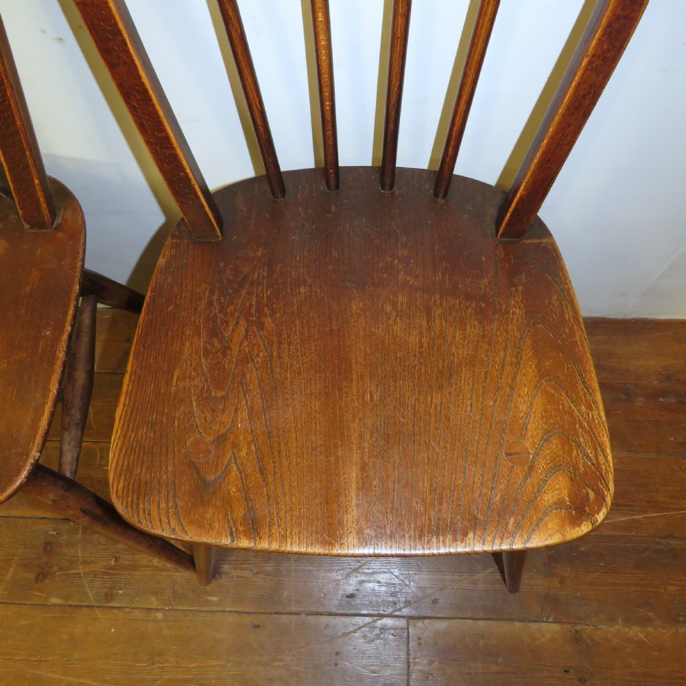 A pair of warm brown wooden dining chairs featuring hoop-shaped spindle backs, contoured elm seats, and splayed legs. View XI