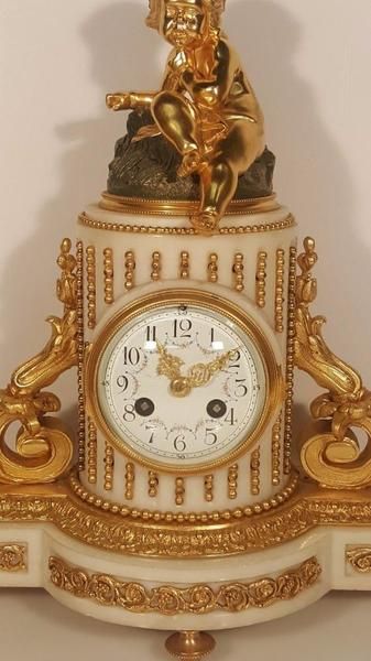 fig 1. A 19th-century French white marble mantel clock decorated with gilded ormolu mounts and topped with a seated cherub figure.