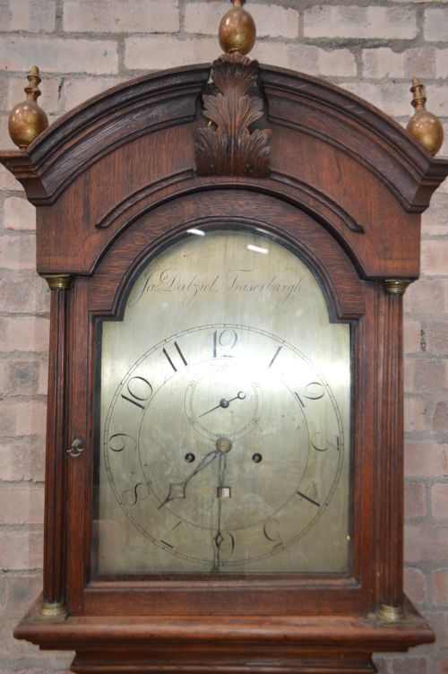 fig 1. A late Victorian Scottish oak longcase clock with an arched hood, carved finials, and an arched painted dial.