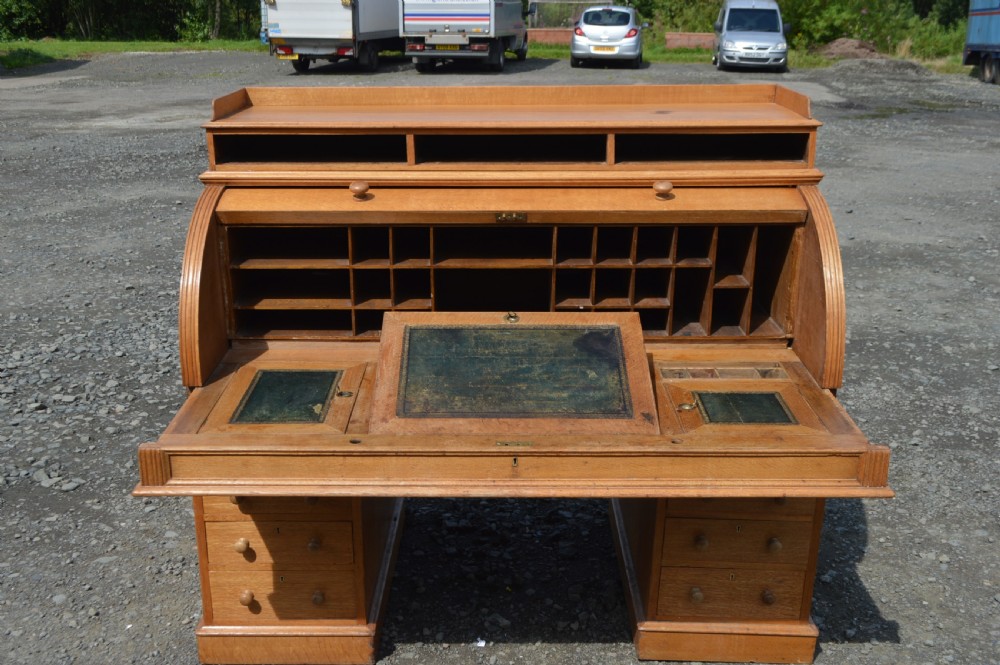 An antique Victorian light oak cylinder desk with a curved roll-top front, twin pedestals containing drawers, and a raised top gallery. View II