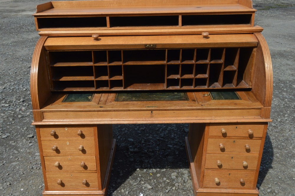 An antique Victorian light oak cylinder desk with a curved roll-top front, twin pedestals containing drawers, and a raised top gallery. View VI