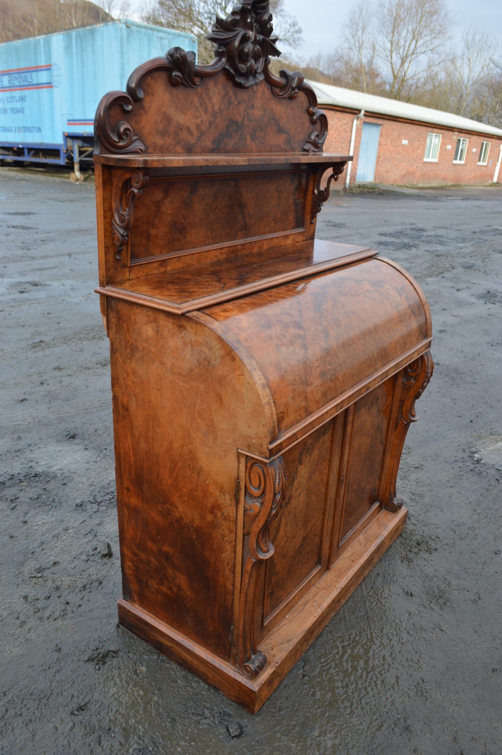 A Victorian burr walnut cylinder front bureau with a carved top pediment, a raised shelf, a curved roll front, and lower cupboard doors. View II