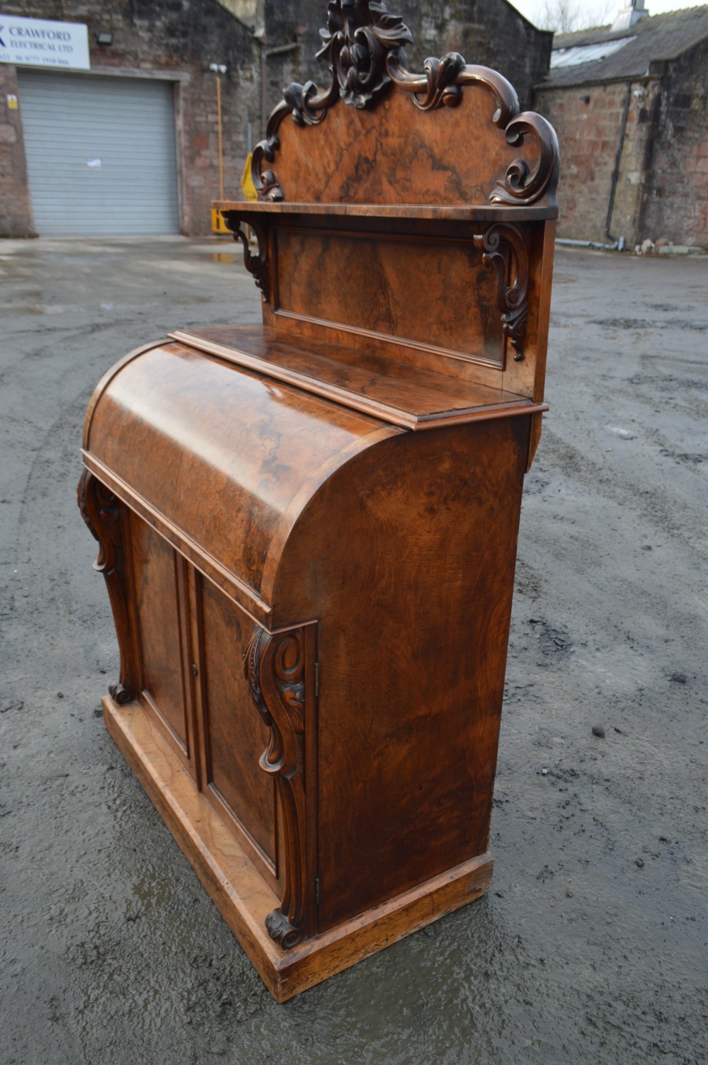 A Victorian burr walnut cylinder front bureau with a carved top pediment, a raised shelf, a curved roll front, and lower cupboard doors. View III